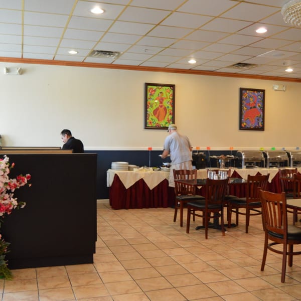 A man serves himself from a buffet line in a brightly lit Indian restaurant dining room.
