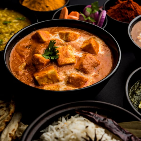 Indian paneer butter masala with cilantro, surrounded by other Indian dishes and spices.