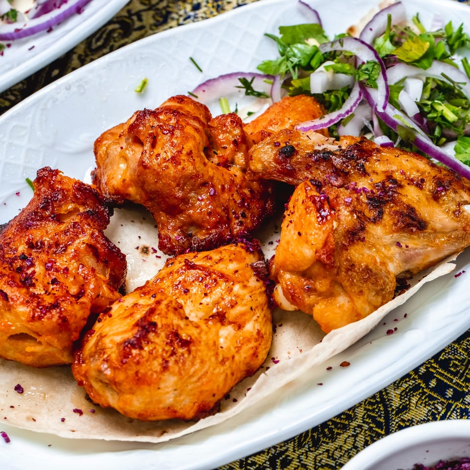 Indian chicken tikka pieces with red onions and herbs on a white plate at Pepper House Township.