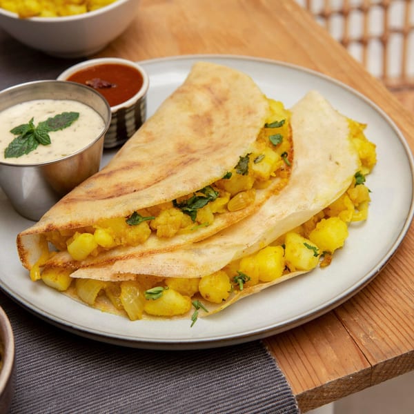Two Indian dosas filled with spiced potatoes and herbs, served with two dipping sauces.