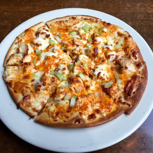 A sliced chicken pizza with melted cheese, orange sauce, and green celery on a white plate.