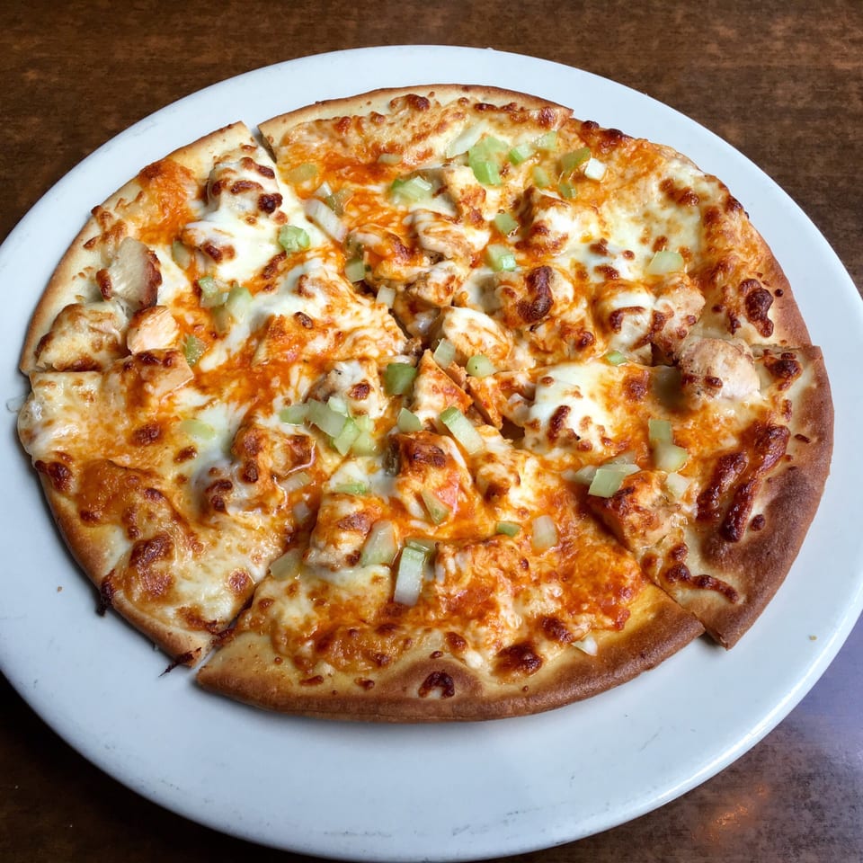 A sliced chicken pizza with melted cheese, orange sauce, and green celery on a white plate.